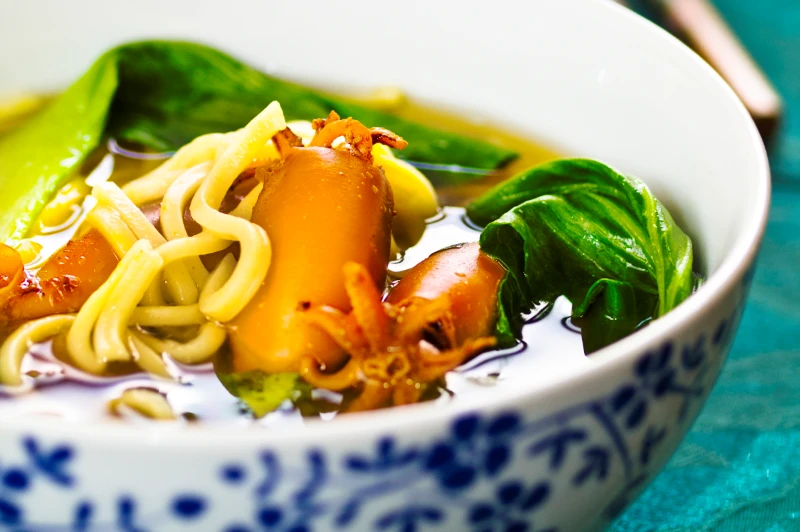 A bowl of noodles and food in soup. 